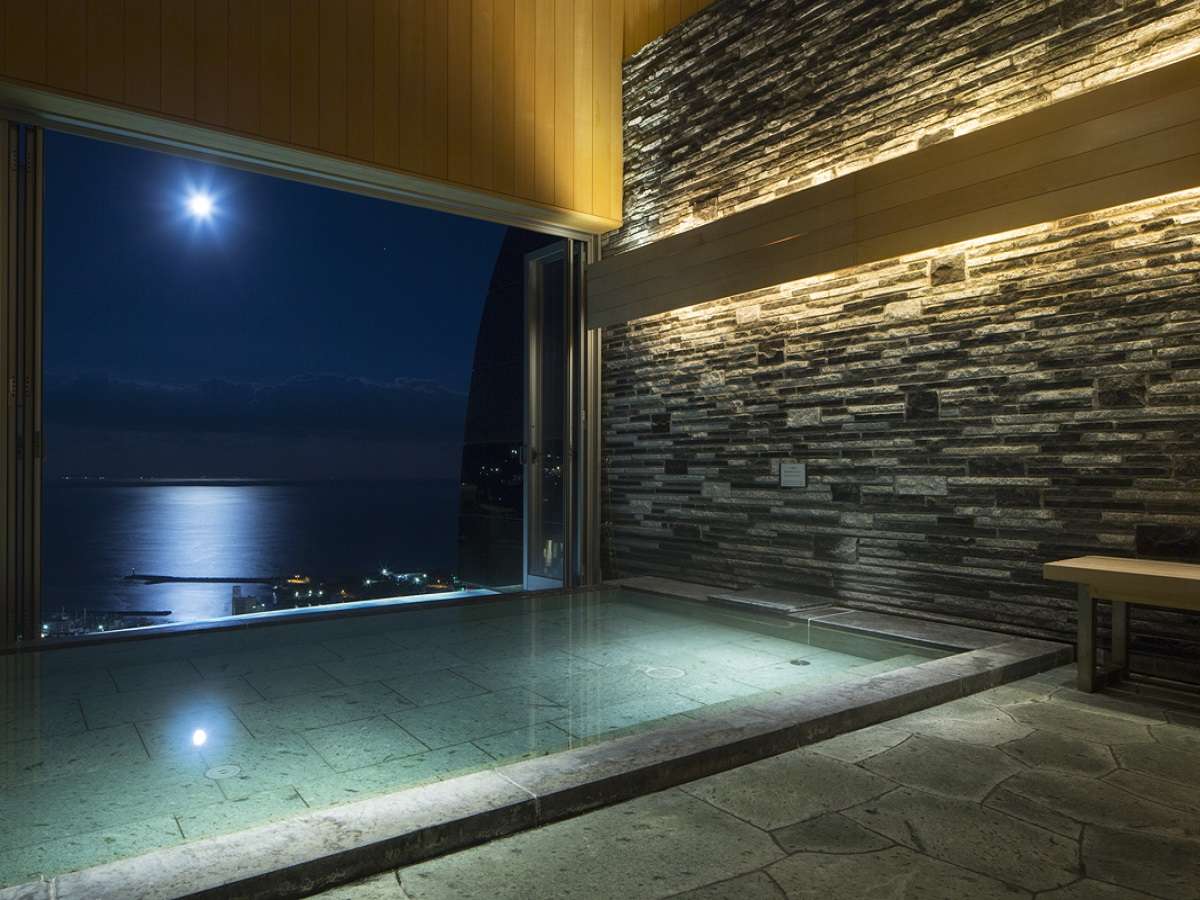 Outdoor stone onsen bath at Risonare Atami with a moonlit view across Atami Bay
