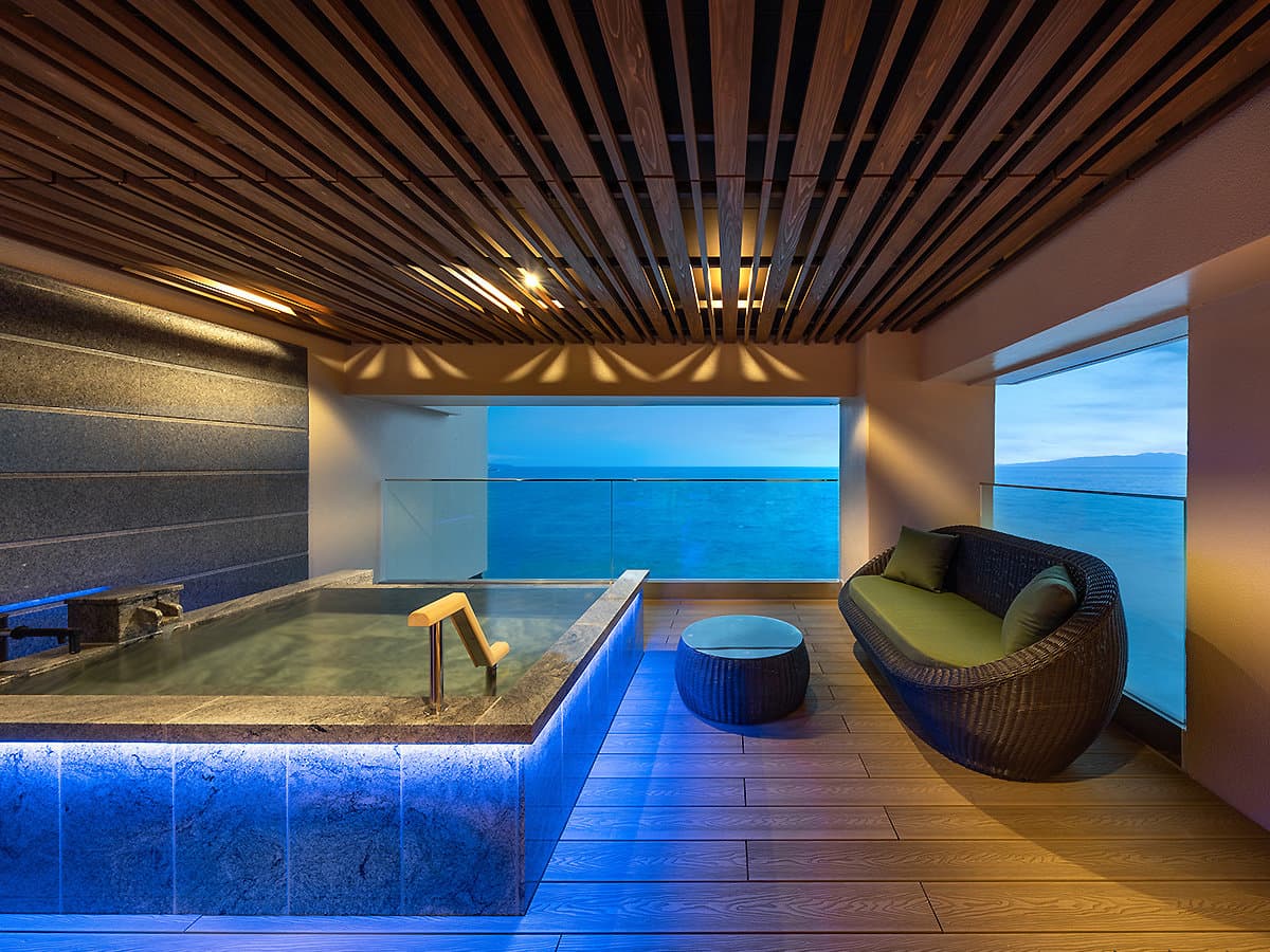 In-room private stone bath with floor-to-ceiling ocean view at dusk at Hama no Yu, Inatori Onsen
