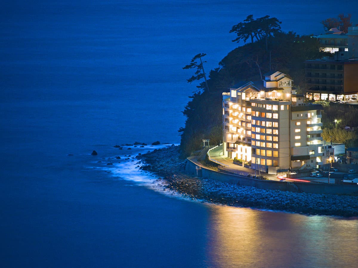 Taberu Oyado Hama no Yu illuminated on the Inatori coast at dusk, the ryokan glowing above the sea in Izu