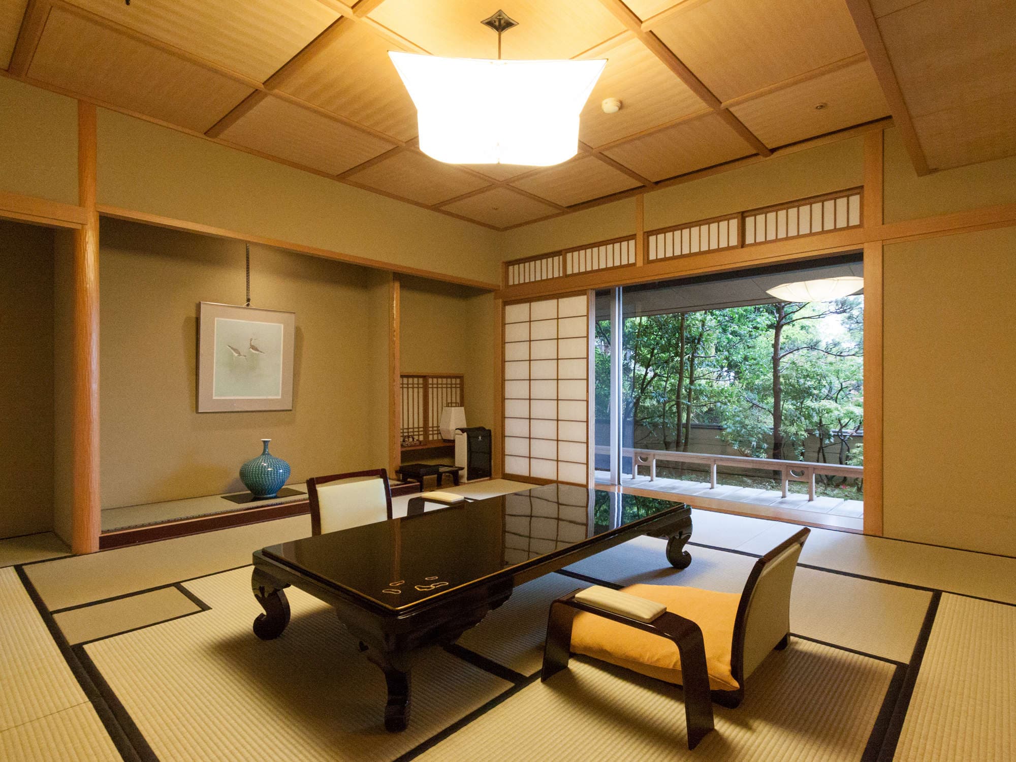 Spacious tatami guest room with low lacquer table and shoji opening to a green garden at Seizan Yamato, Ito Onsen