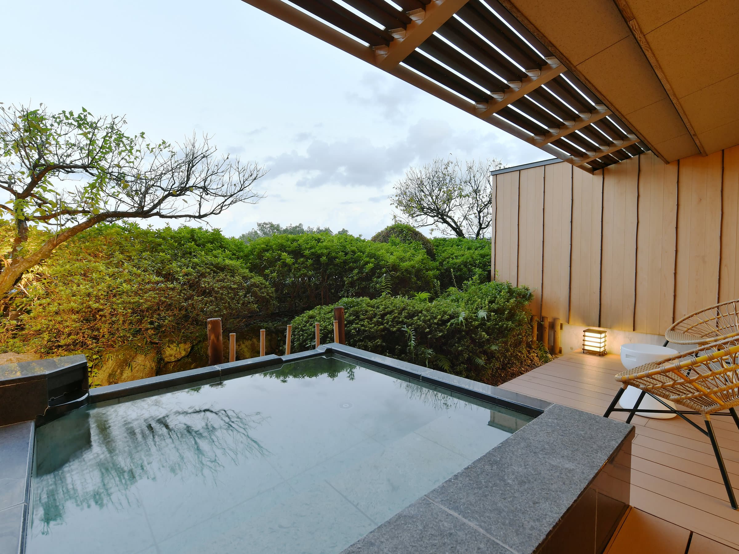 Private open-air stone bath on a guest-room terrace overlooking trees at dusk, Seizan Yamato, Ito Onsen
