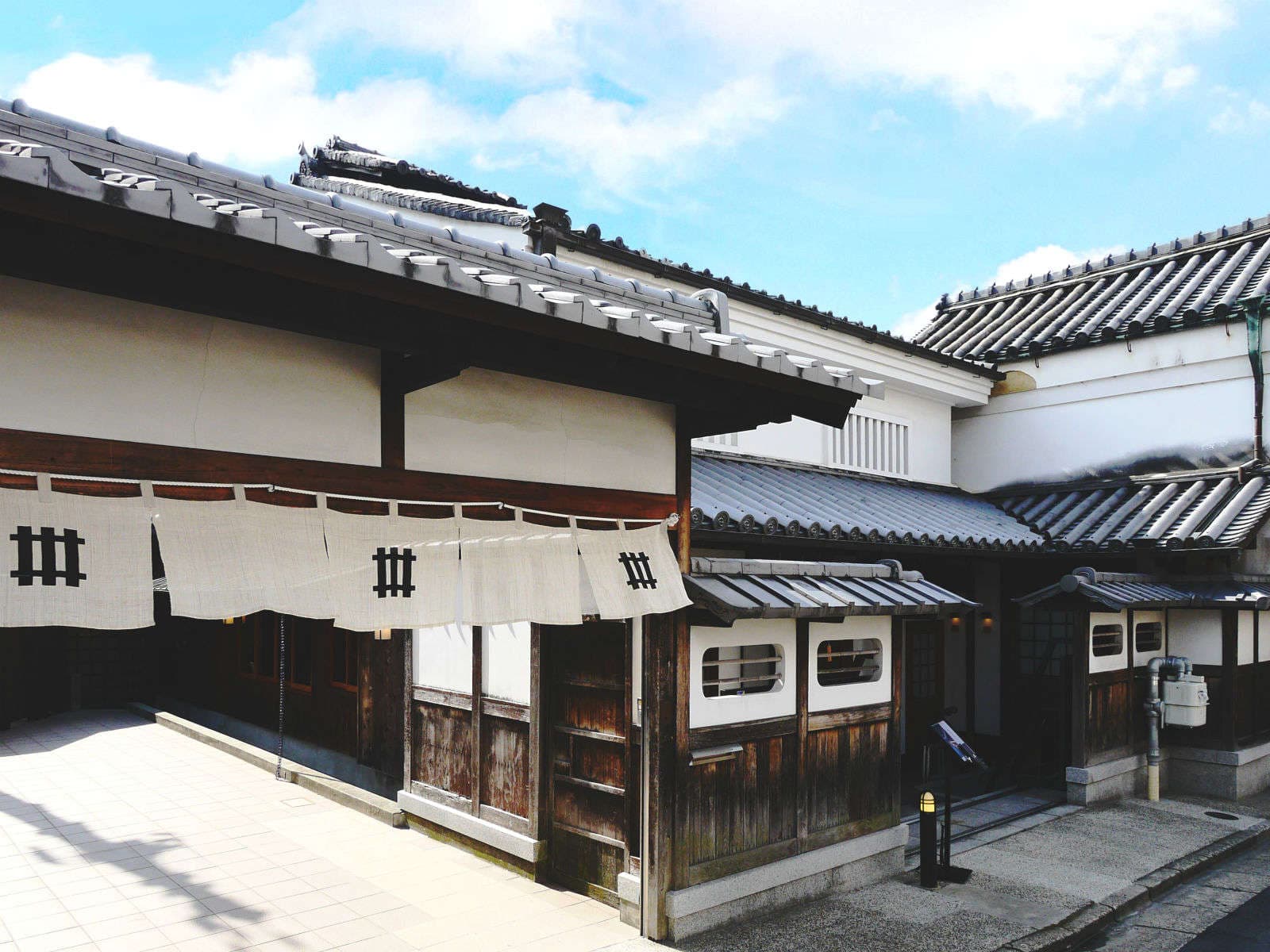 Daytime courtyard of Kaze no Naramachi with white noren curtains and tiled machiya roofs under a blue sky in Nara