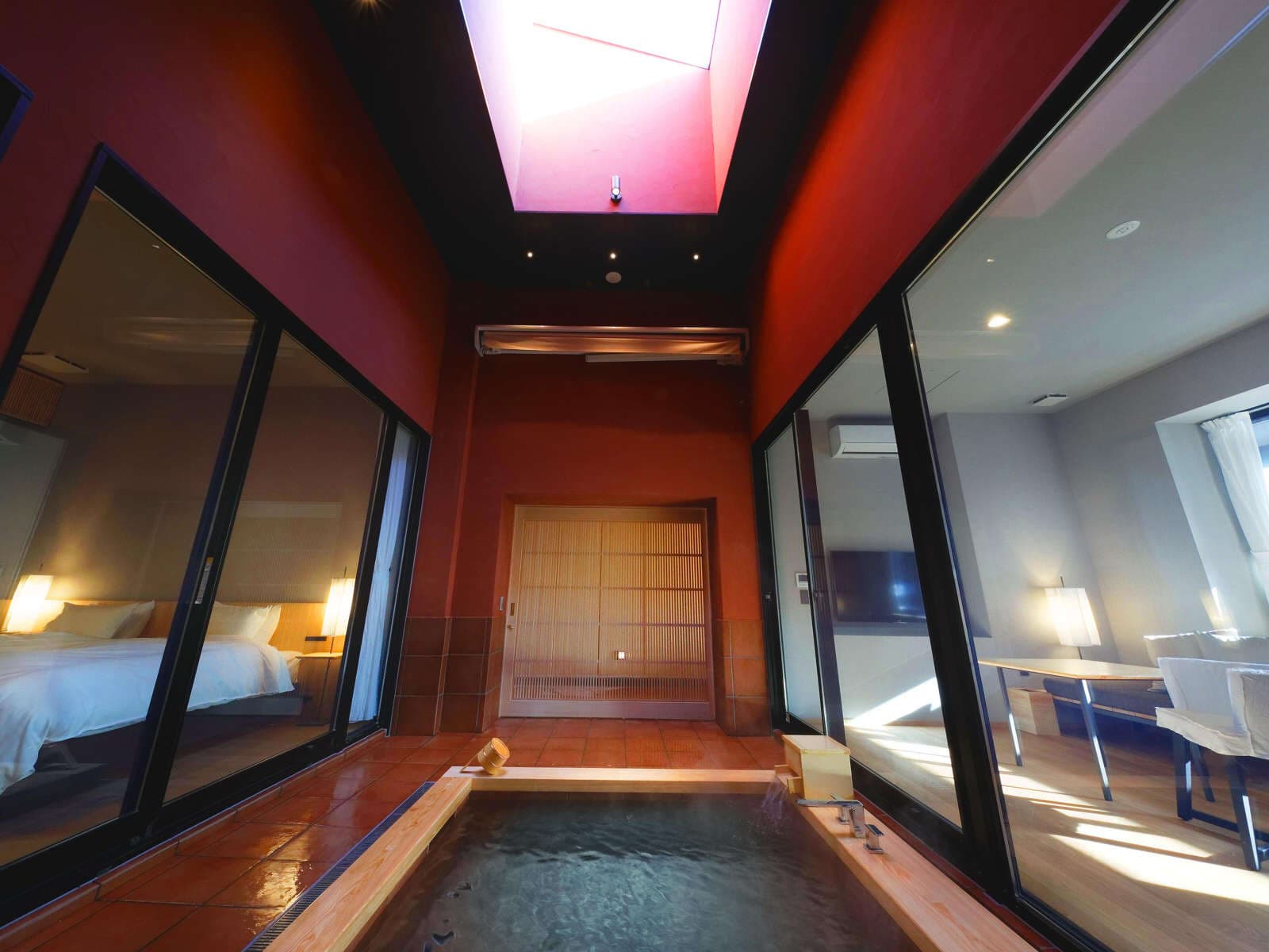 In-room private hot spring bath beneath a skylight in a deep-red walled suite at Koto no Niwa, Dogo Onsen