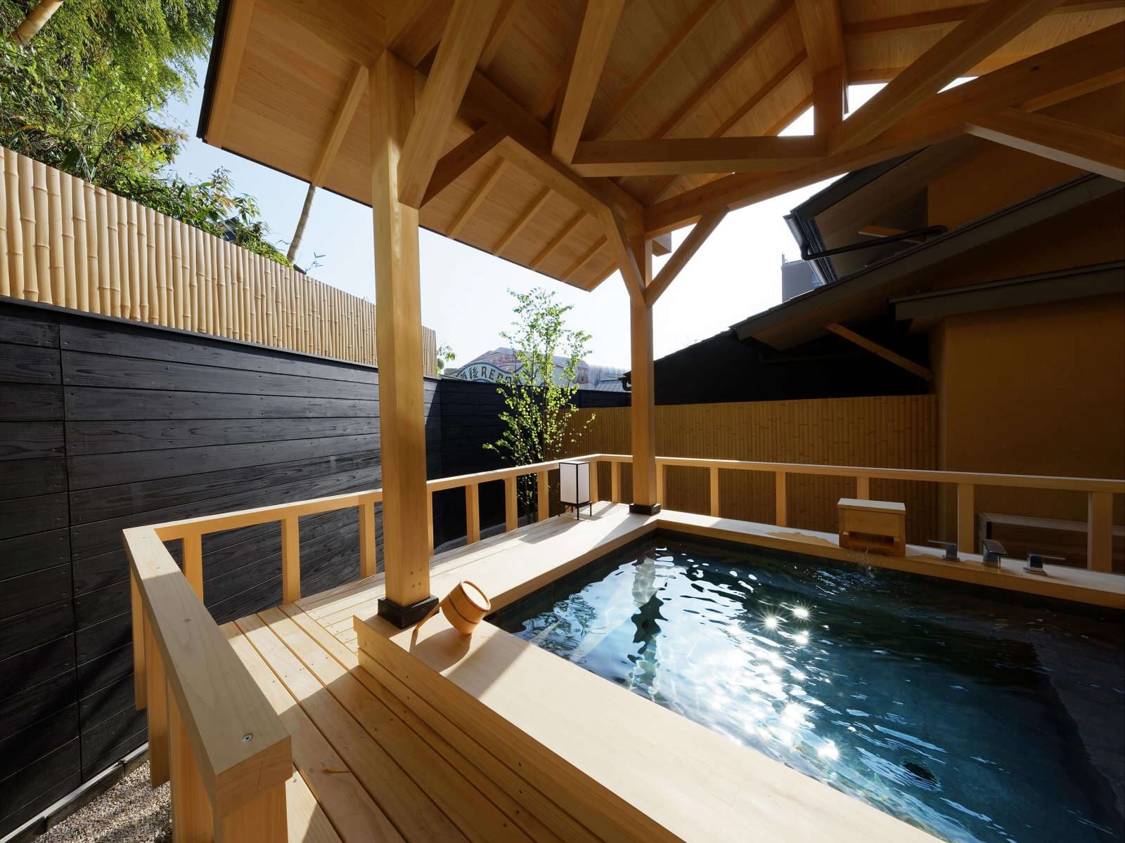 Open-air cypress rotenburo bath under a wooden roof framed by bamboo at Koto no Niwa, Dogo Onsen