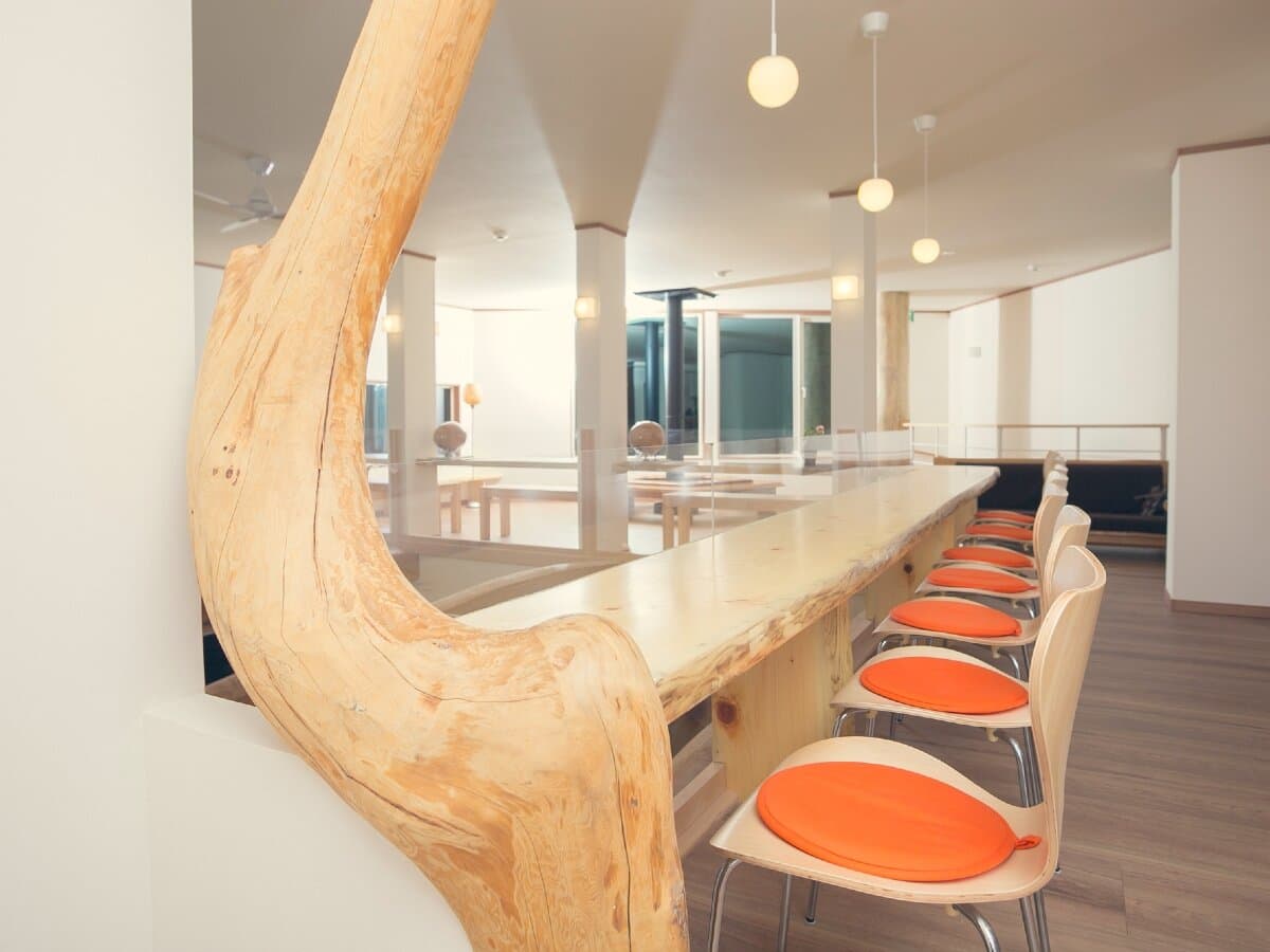 Lounge bar counter made from a live-edge wood slab with orange-cushioned chairs at Ryokan Mokuzin, Hakuba