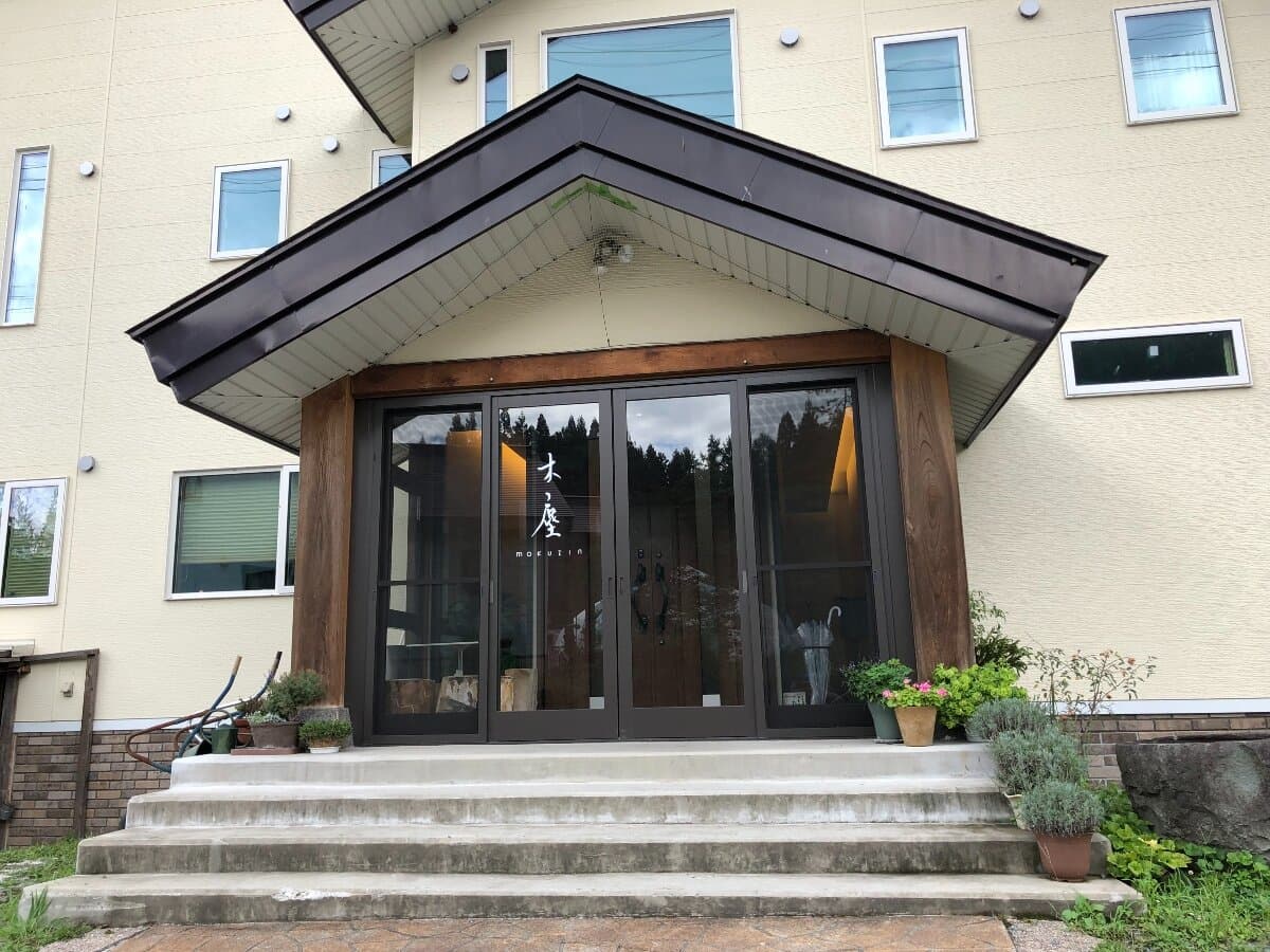 Entrance of Ryokan Mokuzin with wood-framed glass doors and 'mokuzin' name plaque, Hakuba