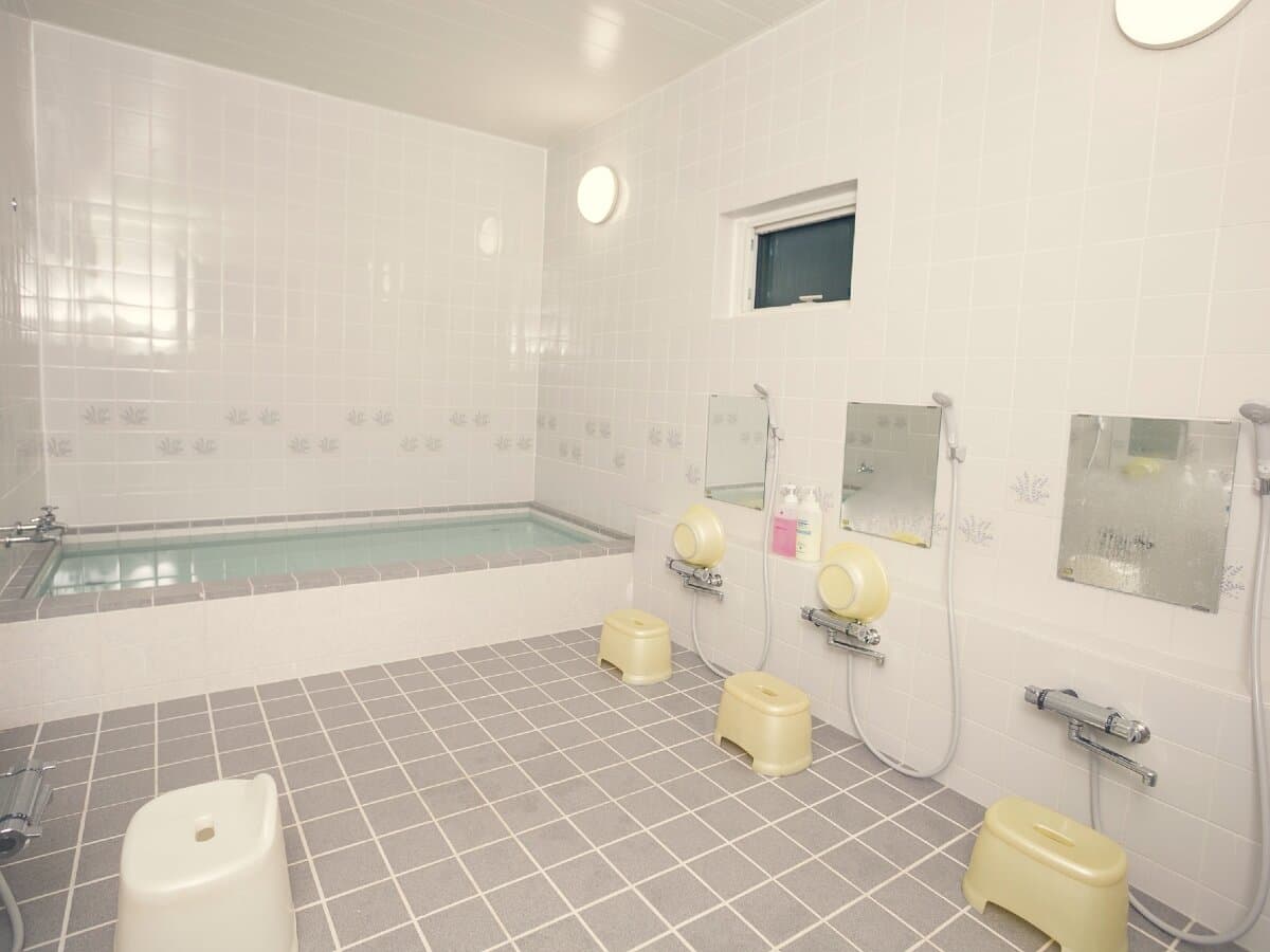 Bright tiled indoor communal bath with a square tub and shower stations at Ryokan Mokuzin, Hakuba