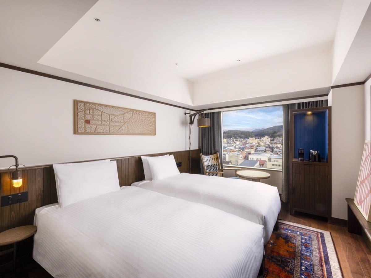 Twin guest room at Mercure Hida Takayama with white bedding, dark walnut walls and a window overlooking Takayama old town