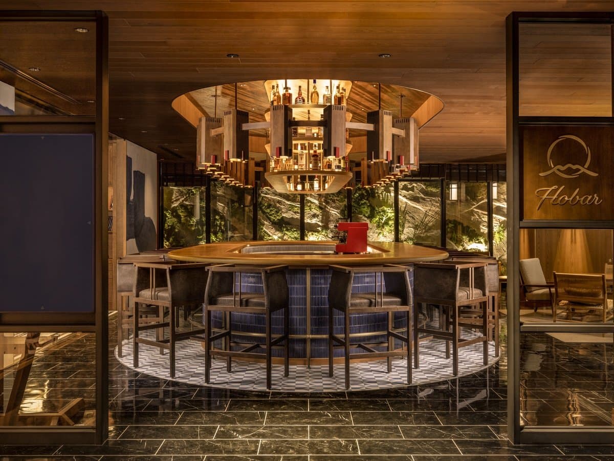 Circular Hobar bar lounge with a statement chandelier, leather stools and a green courtyard view behind