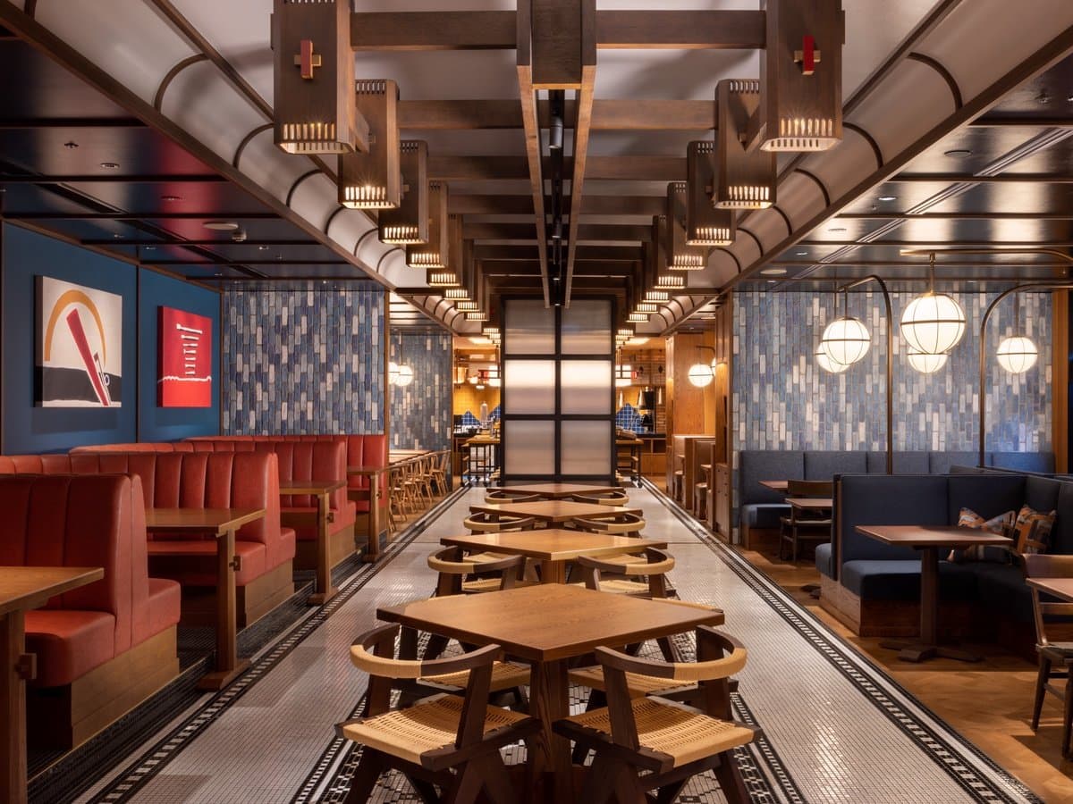 Long restaurant dining hall with picnic-style wood tables, red banquettes and tiled flooring at Mercure Hida Takayama