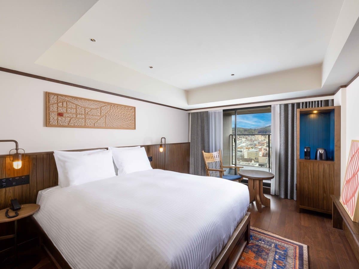 King guest room with crisp white bedding, walnut headboard and a corner window framing the Takayama townscape and mountains