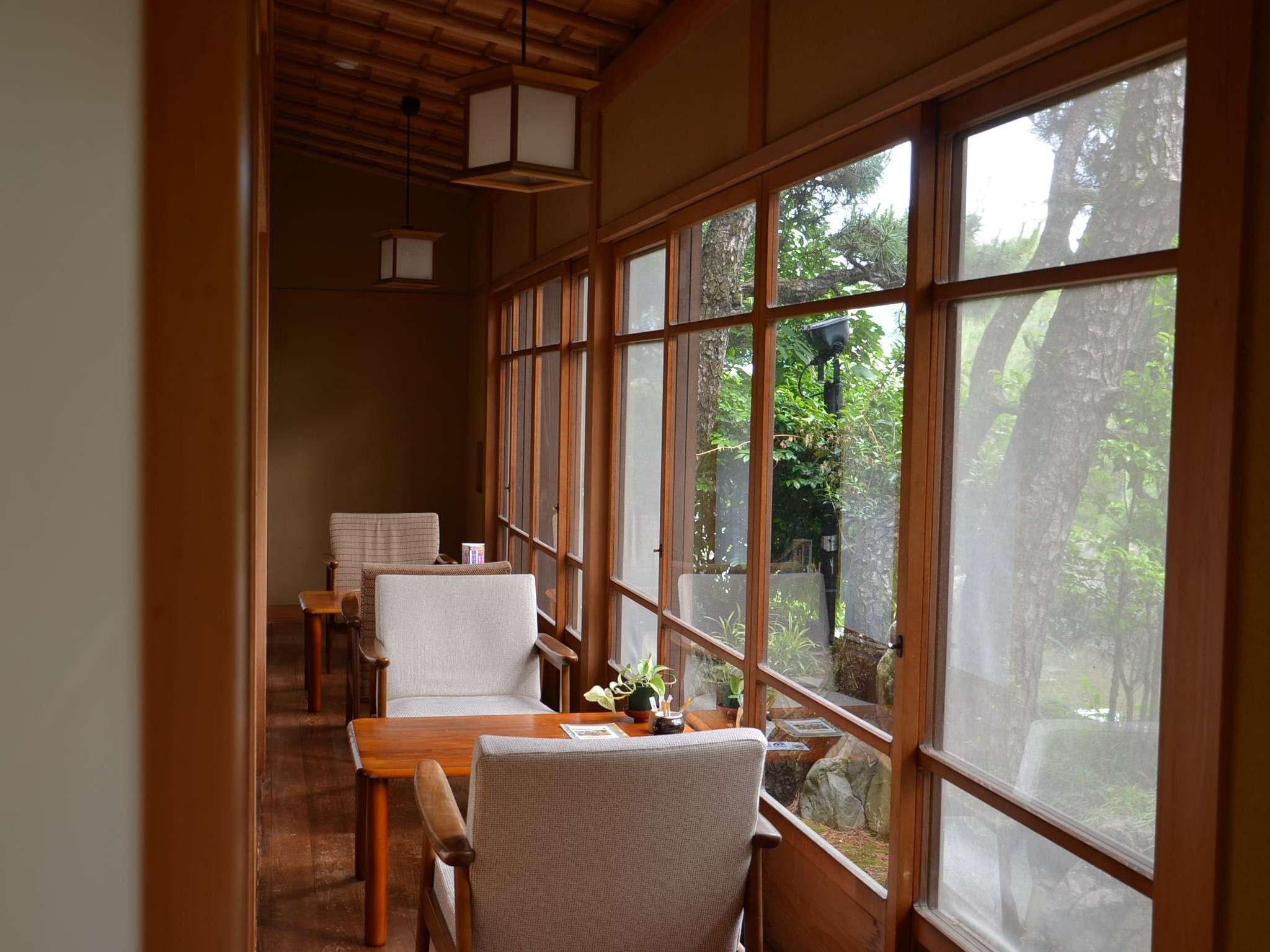 Sunlit wooden corridor lounge with hanging lanterns looking onto the garden at Hotel Dankoen, Ito Onsen