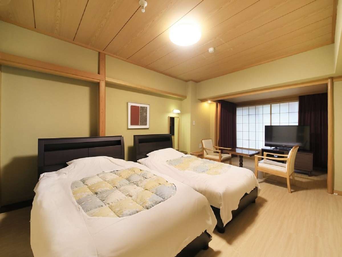 Bright twin-bed guest room with wood ceiling and lounge chairs at Hotel Dankoen in Ito Onsen, Izu