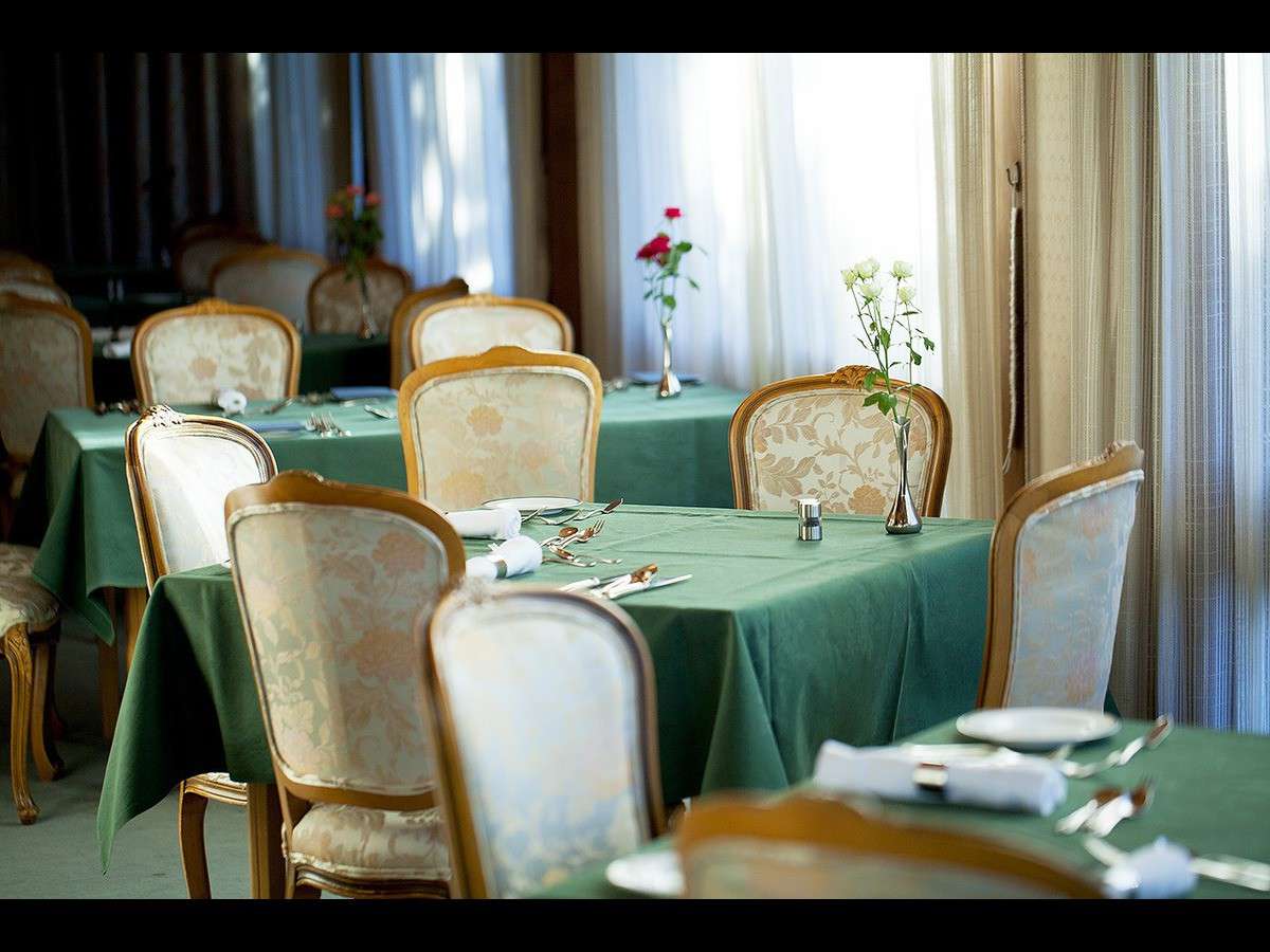 Main dining room at Nara Hotel with green tablecloths, gilt chairs and fresh roses by the windows