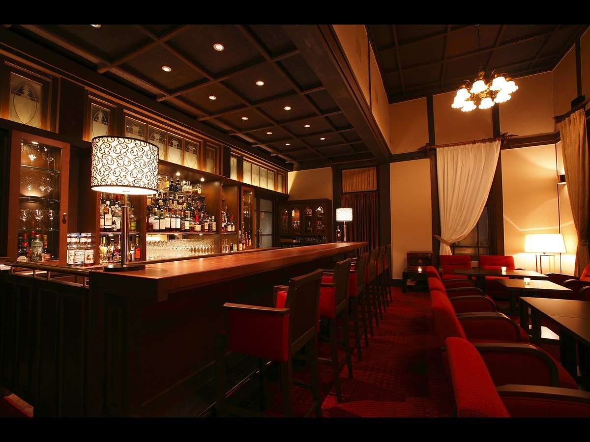 The Bar at Nara Hotel with long wooden counter, red leather stools and warm vintage lighting