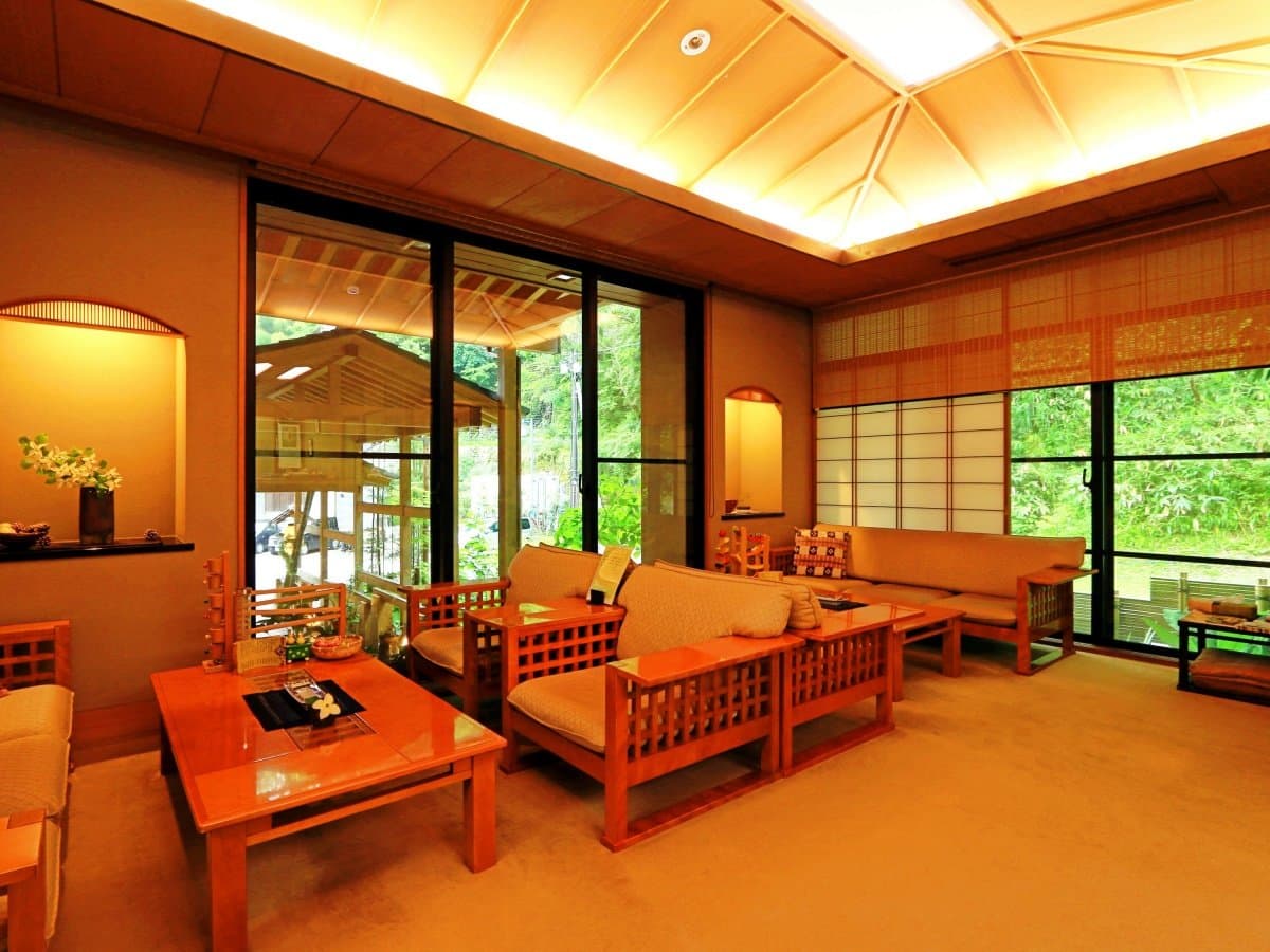 Warmly lit lounge with wooden sofas and garden-facing windows at Oyado Yamashita, Yuwaku Onsen