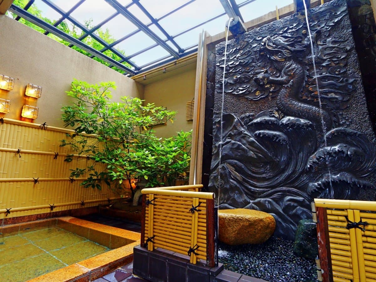 Outdoor stone rotenburo bath with bamboo fence and carved relief wall at Oyado Yamashita, Yuwaku Onsen