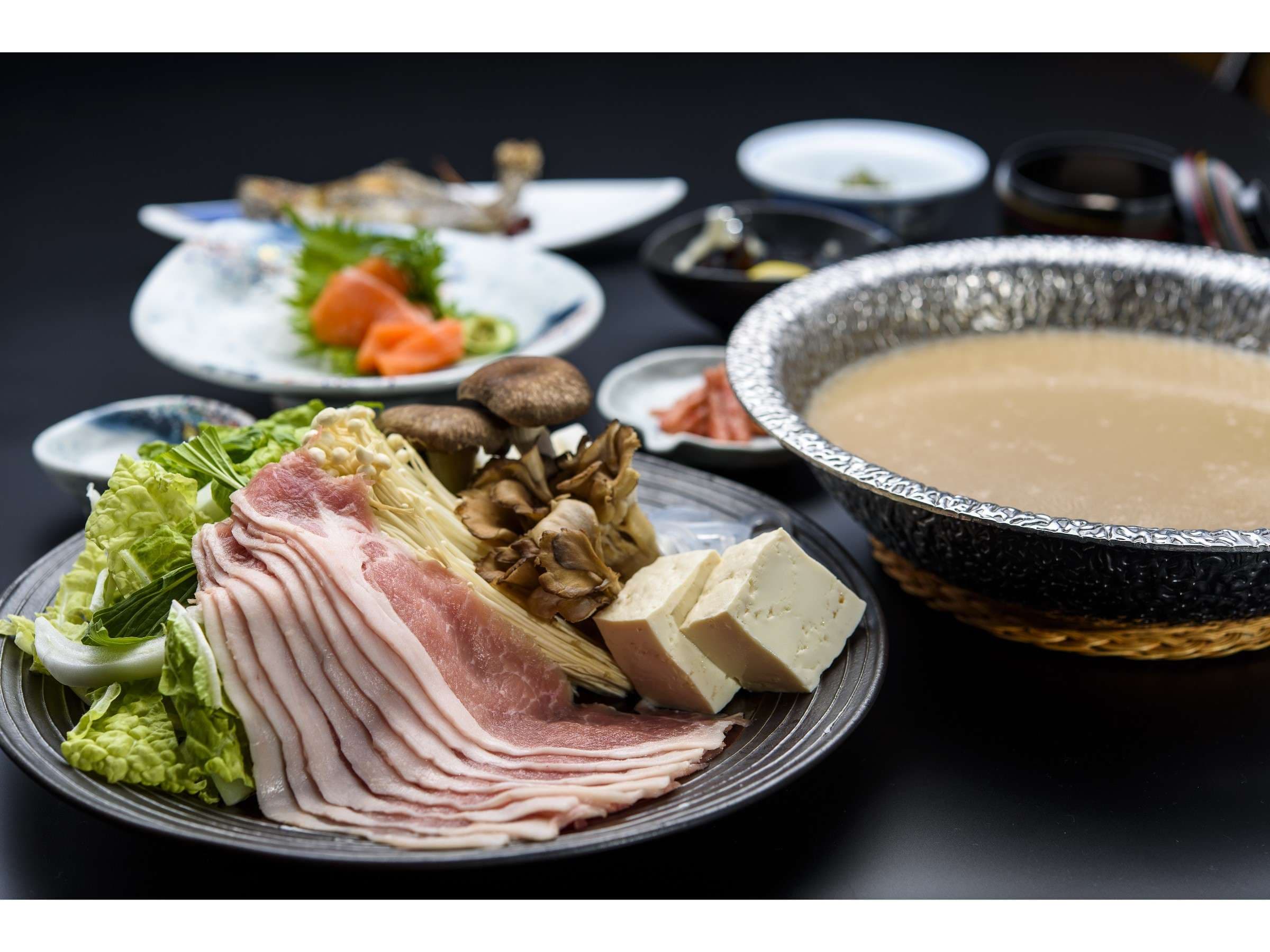 Kaiseki dinner spread at Sansuikan Yugawaso with a milky-broth nabe hot pot, sliced pork, mushrooms, tofu and sashimi
