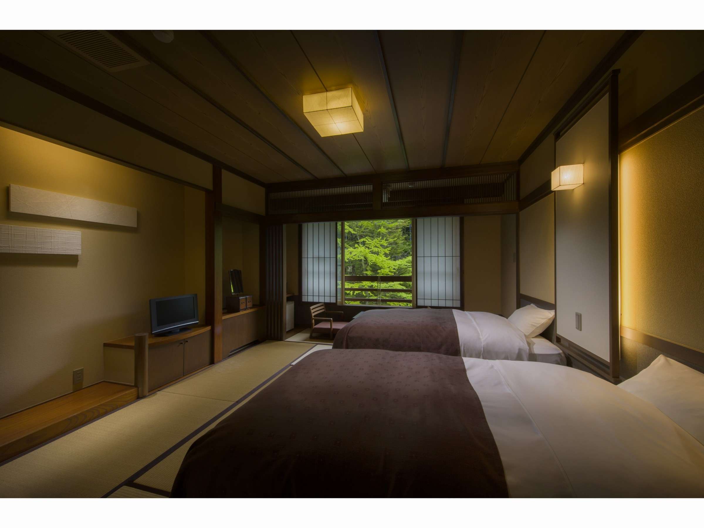 Japanese-Western guest room at Sansuikan Yugawaso with twin beds, tatami and a window framing forest greenery at dusk