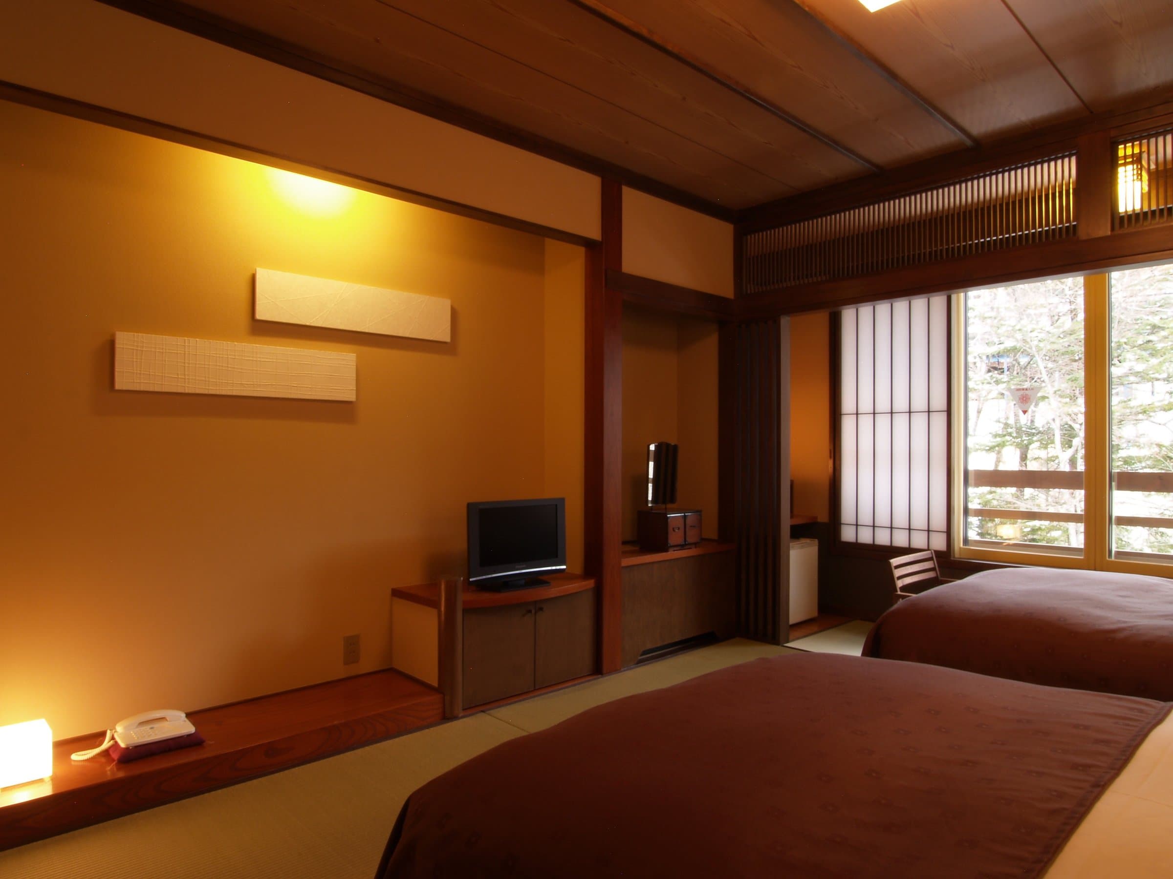 Spacious tatami guest room at Sansuikan Yugawaso with low table, wood lattice transom and a large garden-view window