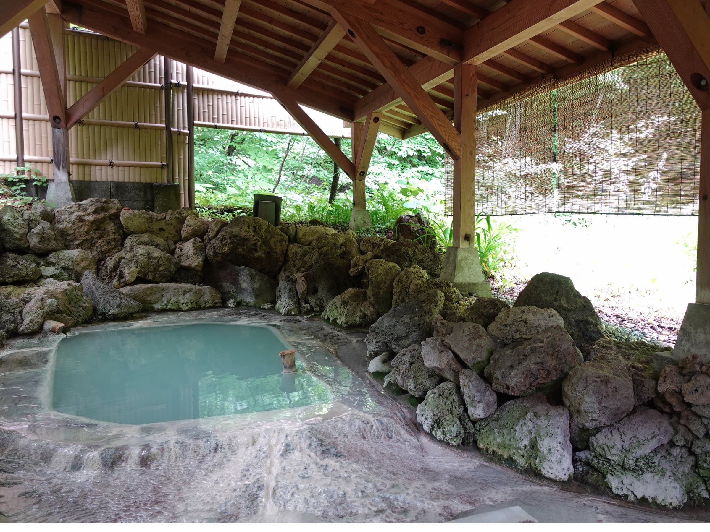 Rock-edged covered open-air bath at Sansuikan Yugawaso with milky Shirahone Onsen water under a wooden timber roof