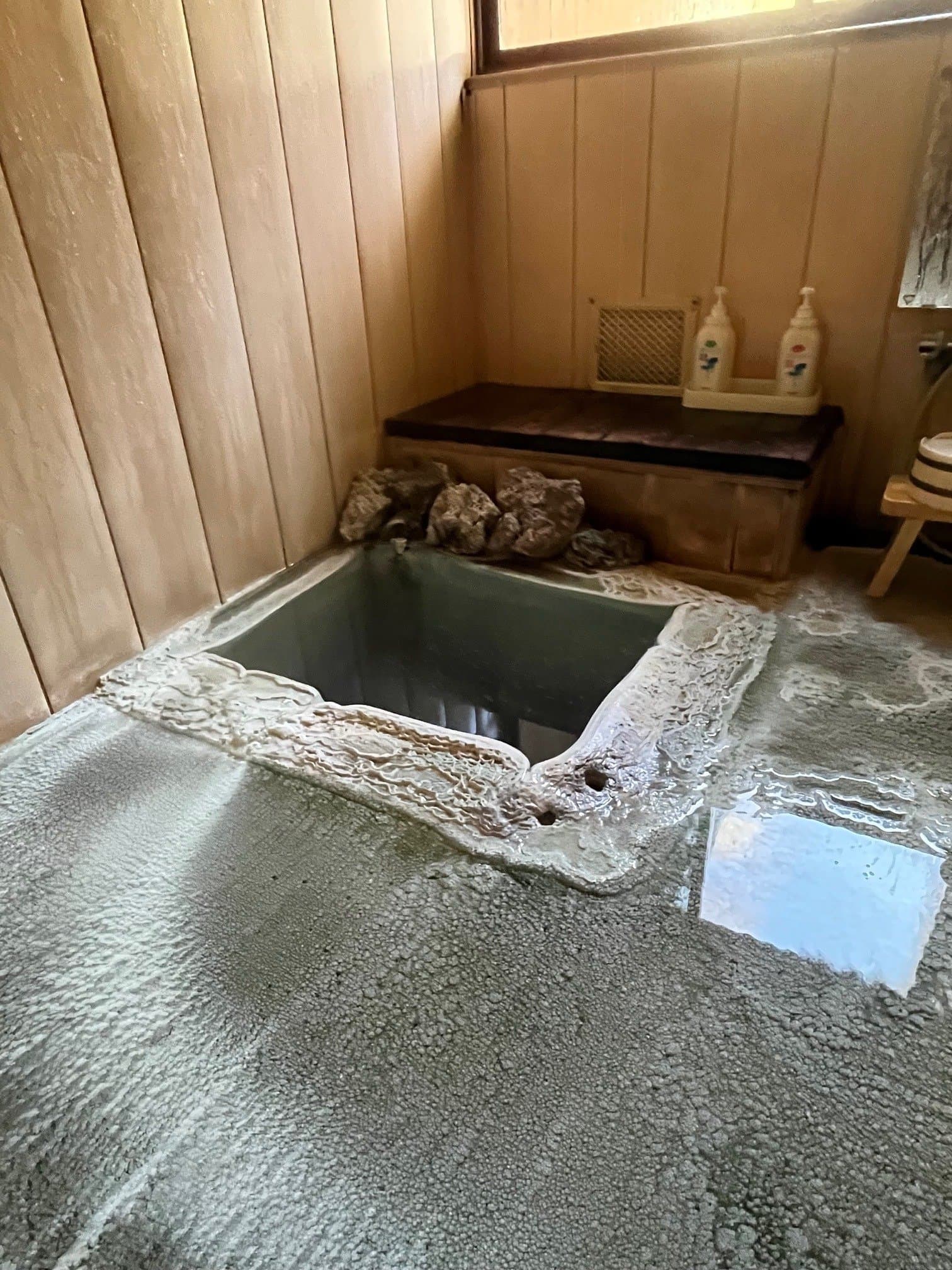 Indoor stone-rimmed bath at Sansuikan Yugawaso with thick mineral deposits and milky Shirahone Onsen spring water