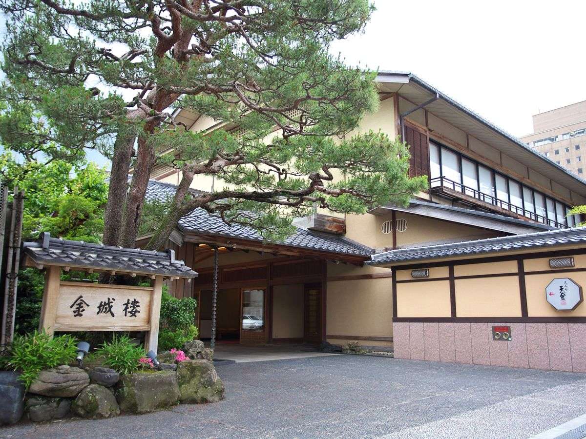 Kinjohro ryotei ryokan main entrance and traditional building lit at dusk amid garden trees in Kanazawa