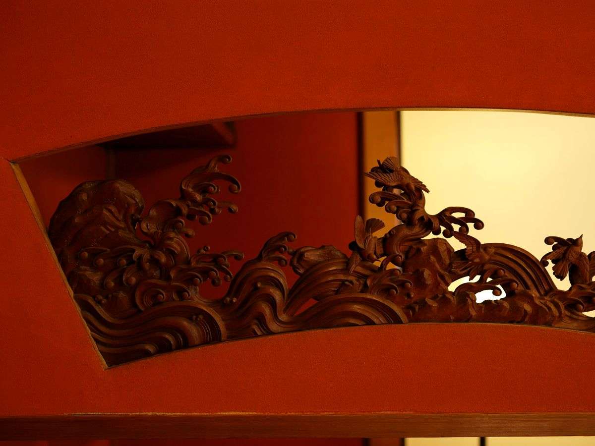 Ornately carved wooden ranma transom detail above a vermilion-walled room at Kinjohro in Kanazawa