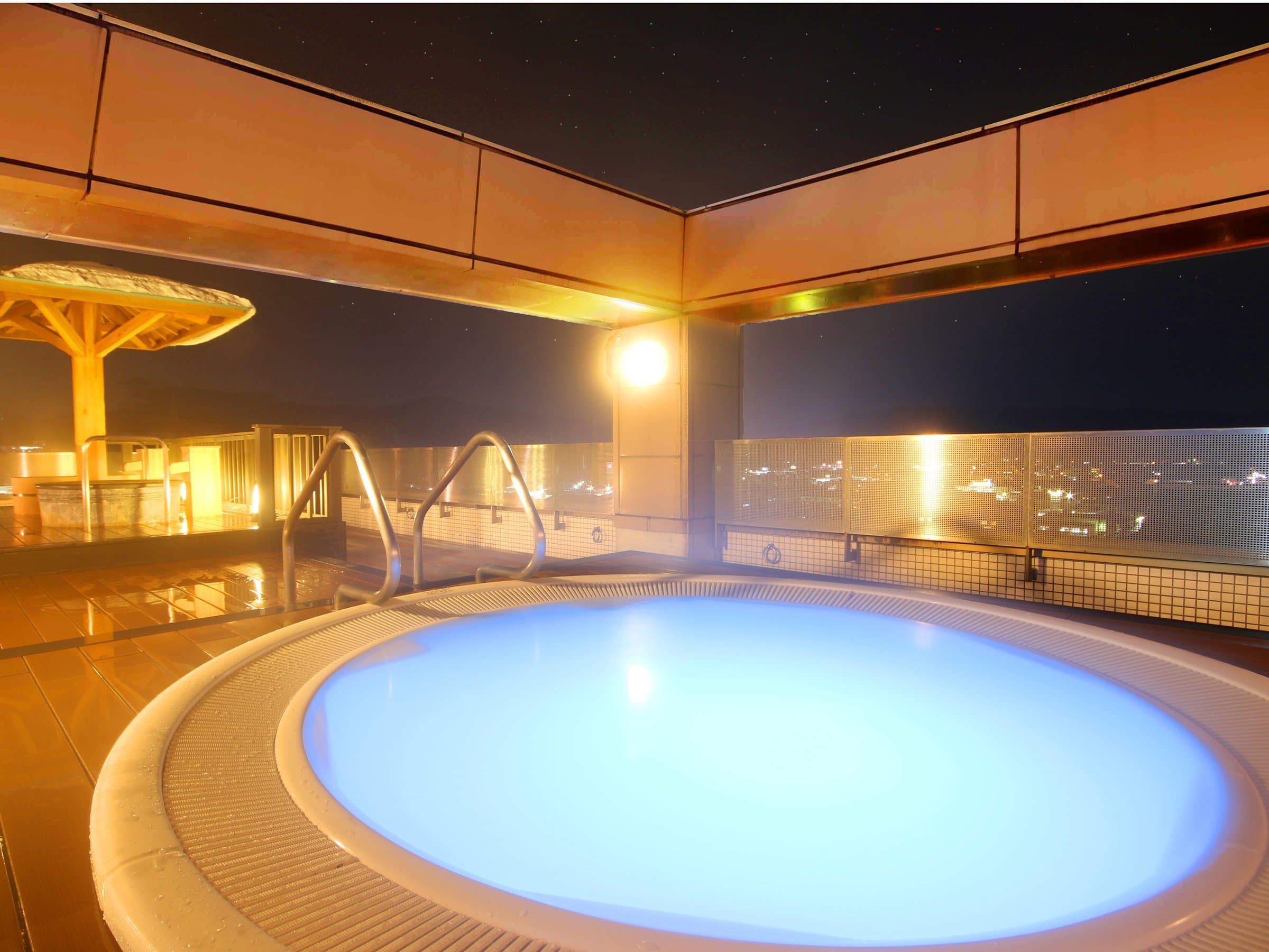 Illuminated rooftop circular open-air bath at Hida Hotel Plaza at night with Takayama city lights beyond