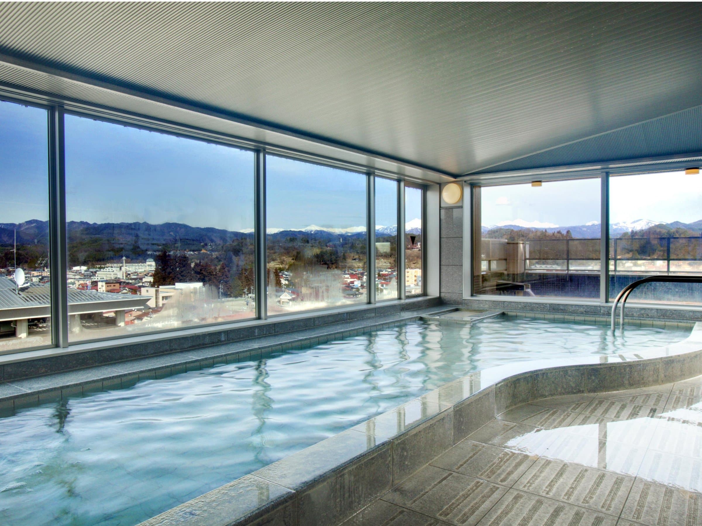 Indoor hot-spring bath at Hida Hotel Plaza with panoramic windows overlooking Takayama town and snow-capped mountains