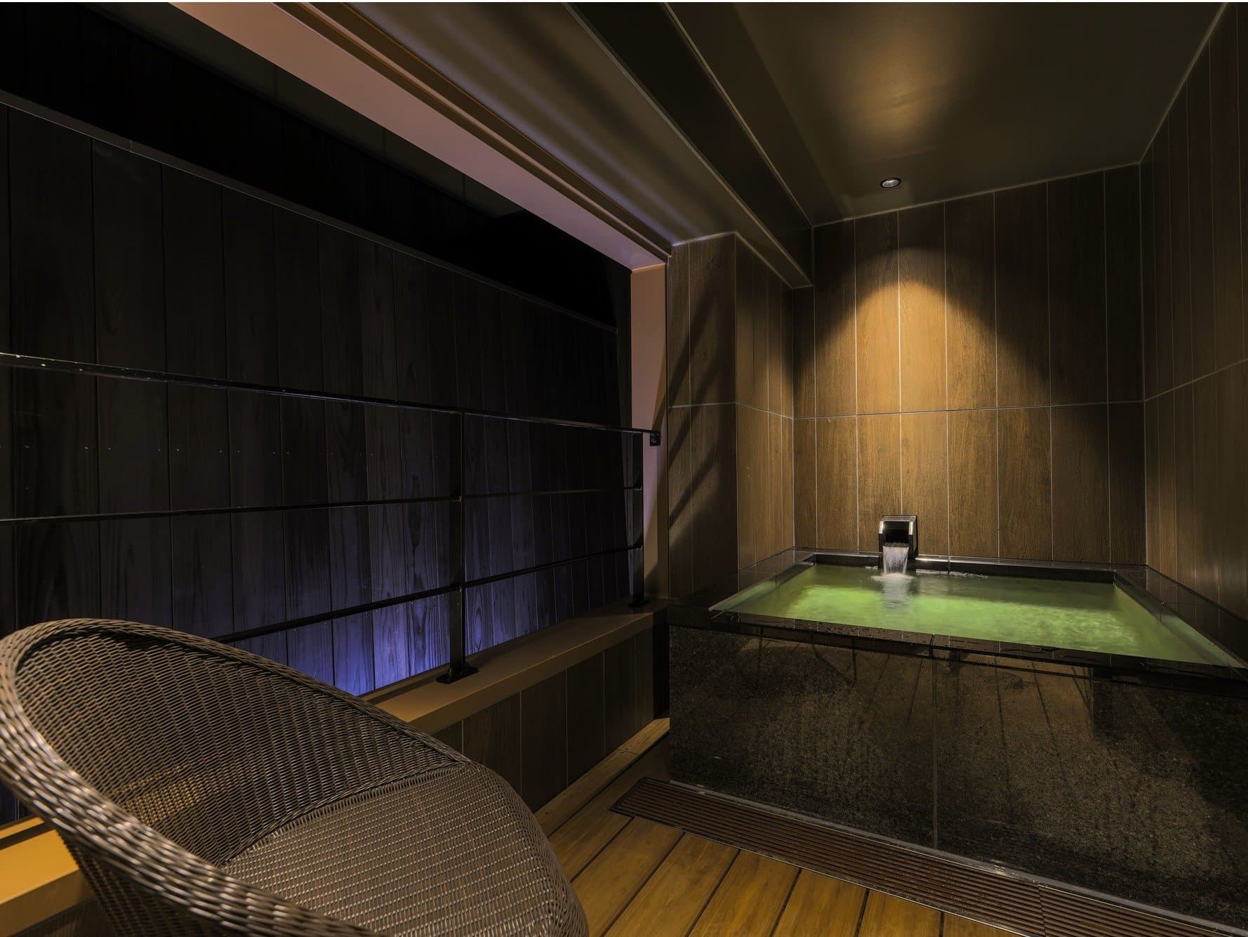 Dark wood private hot-spring bath at Hida Hotel Plaza with a wicker chair and dim accent lighting