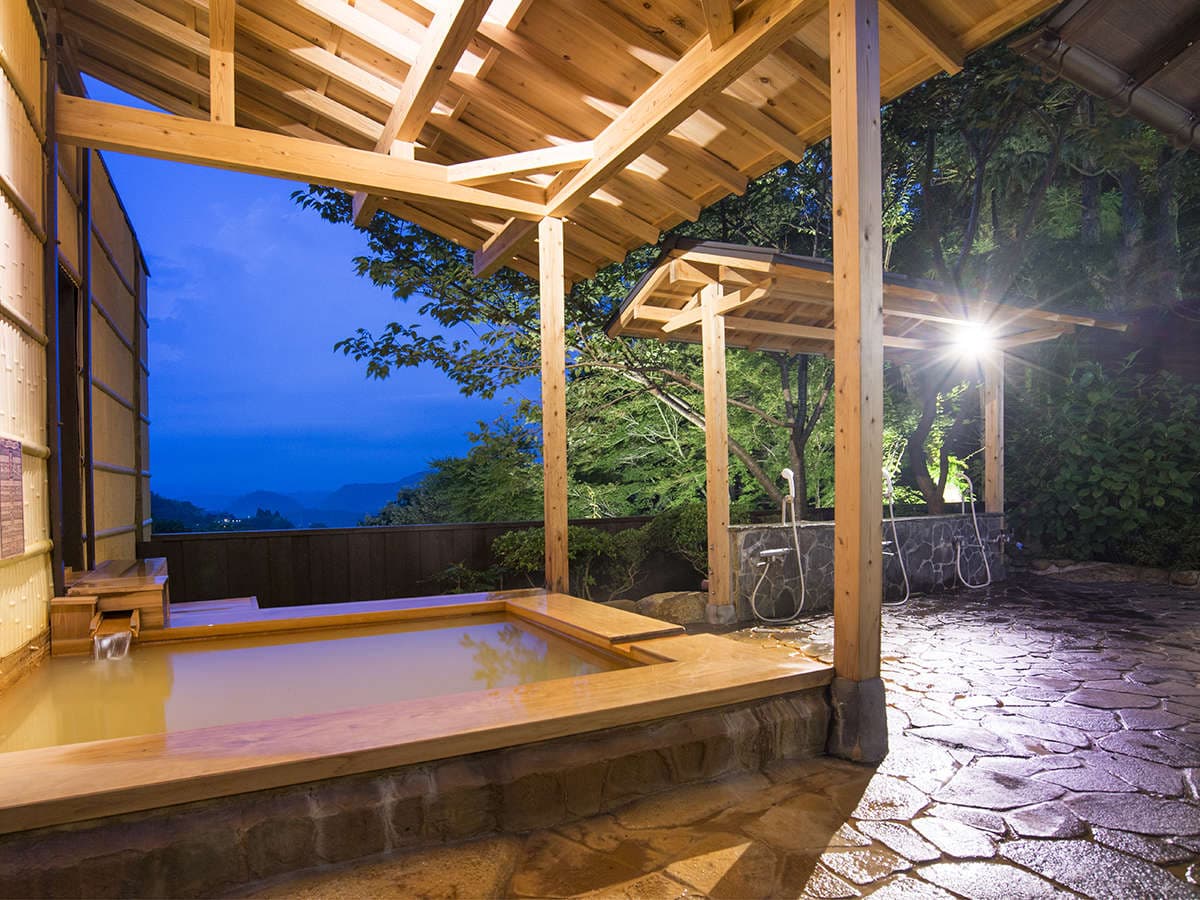 Kinsen gold-spring open-air rotenburo with reddish-brown water under a timber roof at dusk, overlooking the Arima mountains at Motoyu Ryusenkaku