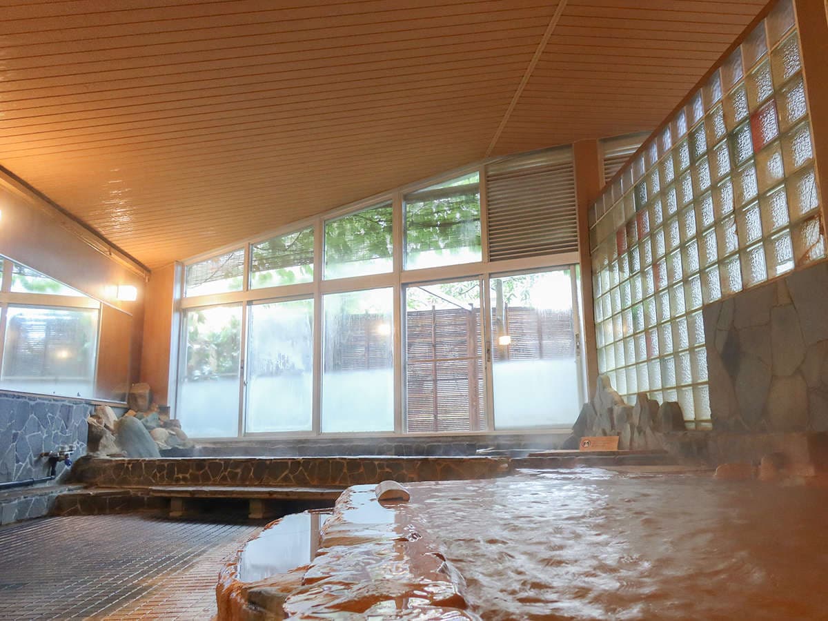 Indoor kinsen gold-spring bath with reddish-amber water, a stone-edged pool and glass-block wall rising with steam at Motoyu Ryusenkaku, Arima Onsen