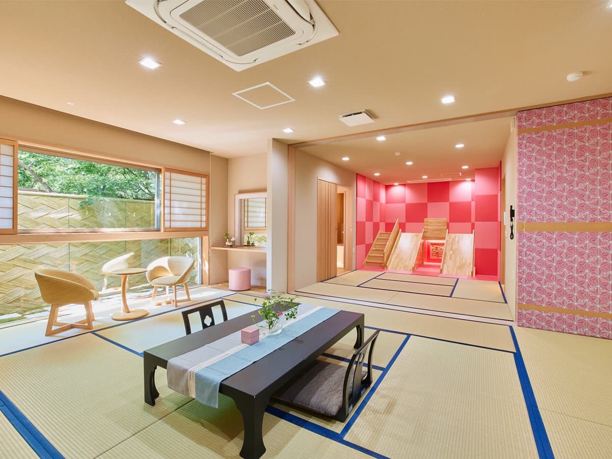 Large family-suite tatami room with a low table, lounge seating by the garden window and an adjoining children's play alcove at Motoyu Ryusenkaku, Arima Onsen