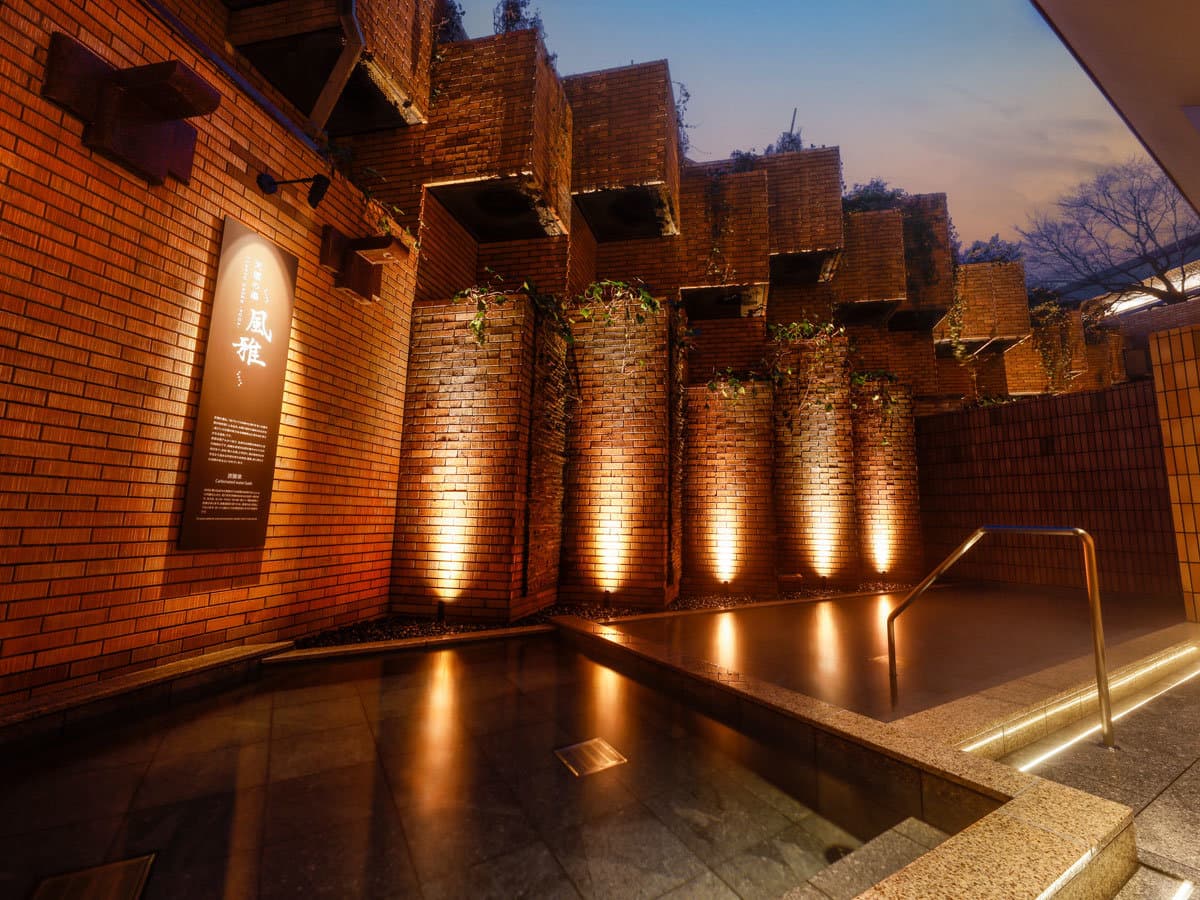 Brick-walled outdoor onsen lit by warm uplights at dusk at Takayama Green Hotel in Hida Takayama