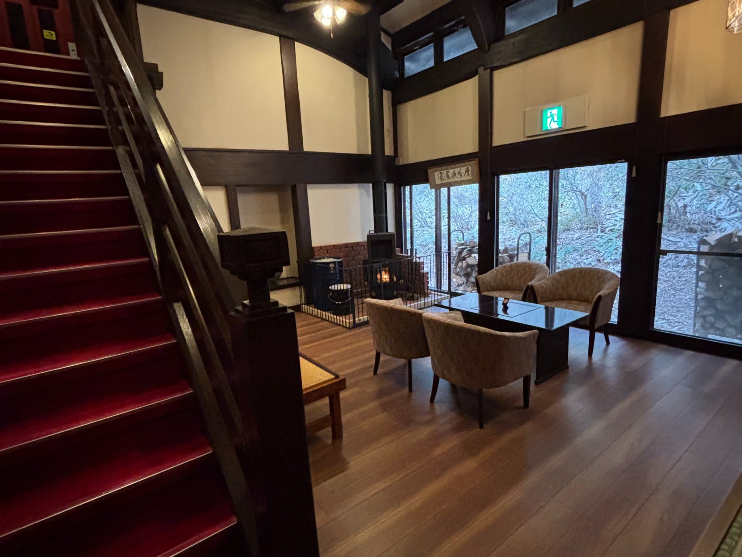 Cosy timber lounge at Ryokan Murayama with red-carpeted staircase, armchairs and a wood-burning stove