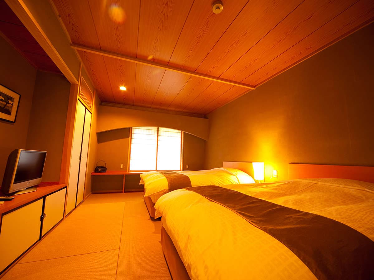 Warmly lit twin-bed Japanese room at Yufuin Hoteiya with wooden ceiling and shoji window