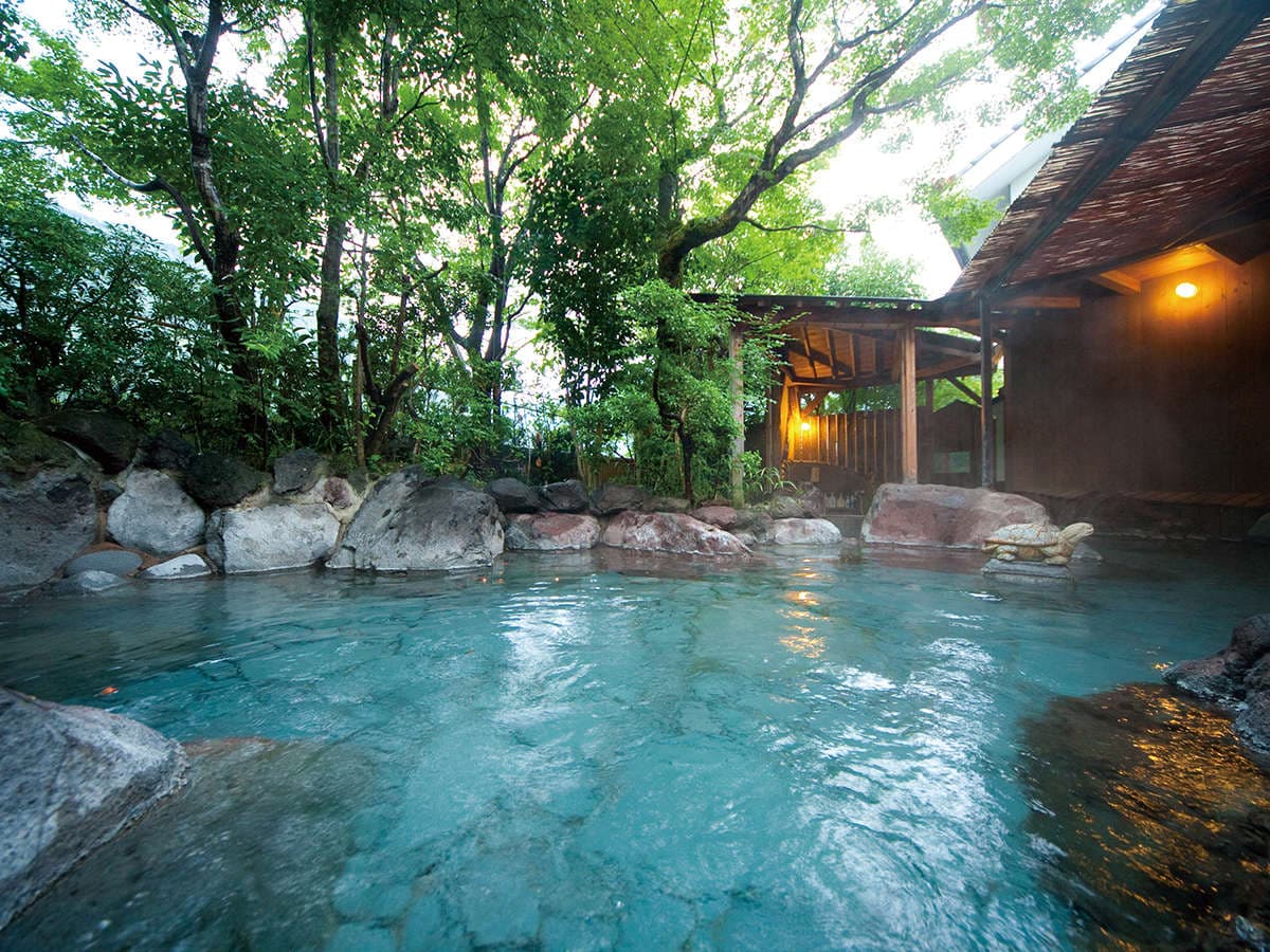 Open-air rotenburo hot spring bath at Yufuin Hoteiya ringed by natural rocks and lush trees