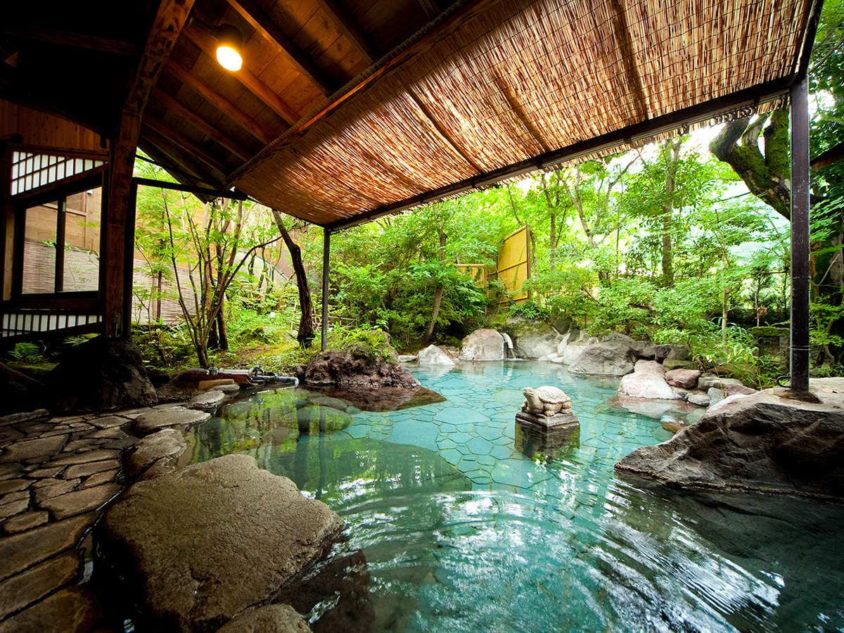 Outdoor onsen at Yufuin Hoteiya under a bamboo-screen roof surrounded by forest greenery