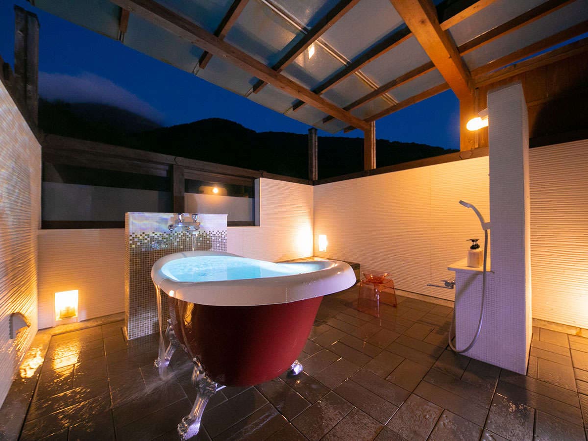 Private open-air bath at Yufuin Hoteiya with a clawfoot tub at dusk and mountains in the distance