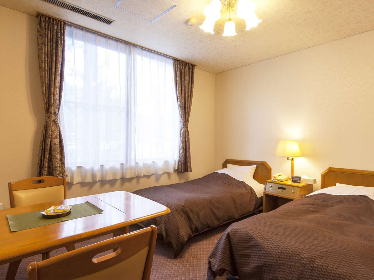 Western-style twin bedroom with two single beds, writing desk and curtained window at Hotel Seikoen in Nikko