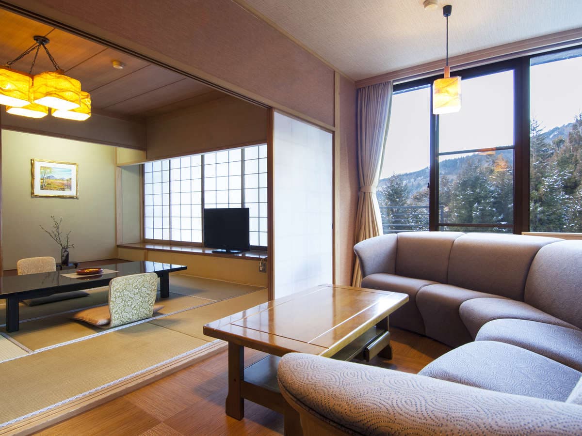 Combined Japanese and Western guest room with sofa lounge and large window framing Nikko mountain scenery