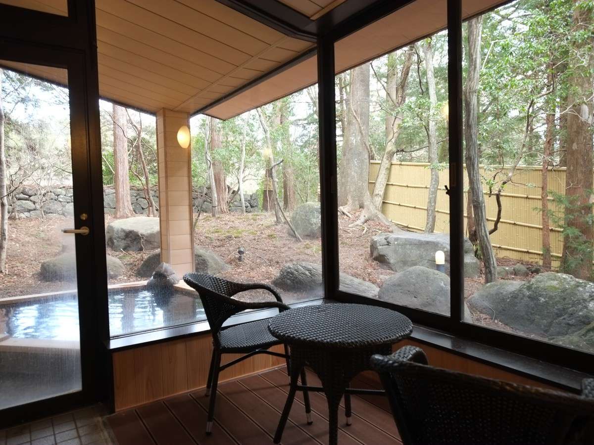 Open-air onsen bath with rattan lounge chairs looking out onto Nikko's forest and stone garden