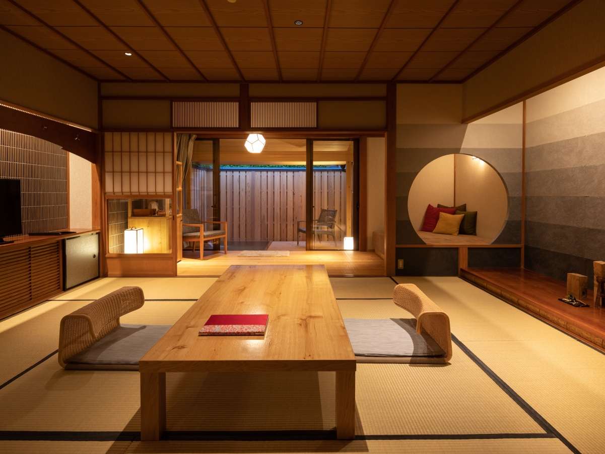 Spacious tatami guest room with low wooden table, floor chairs and a round sitting nook against a striped wall at Yunode Ryokan