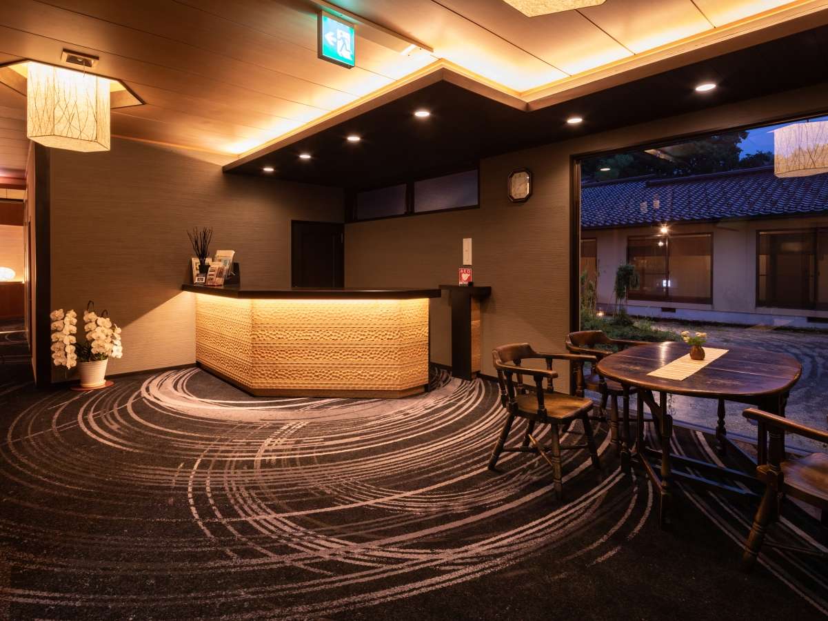 Warmly lit front reception desk with raked-pattern carpet and a garden view at Yunode Ryokan, Yuwaku Onsen