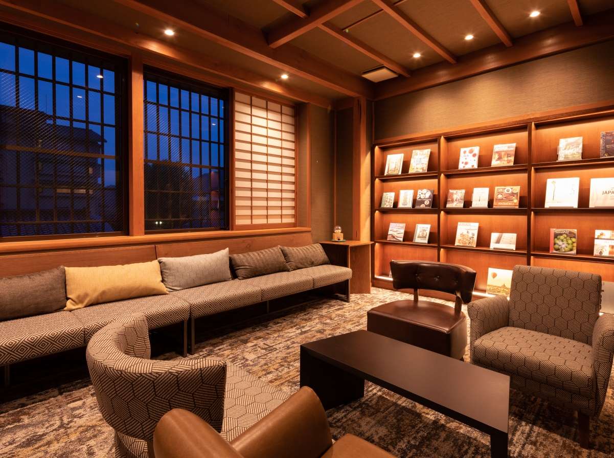 Library lounge with long sofa, shoji windows and shelves of books at Yunode Ryokan in Yuwaku Onsen