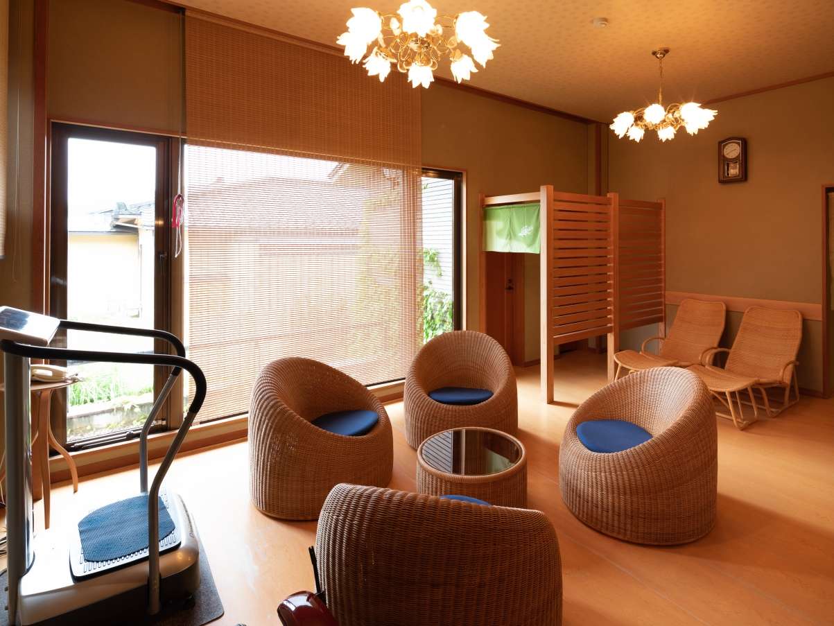 Sunlit post-bath relaxation room with rattan chairs and bamboo blinds at Yunode Ryokan, Yuwaku Onsen