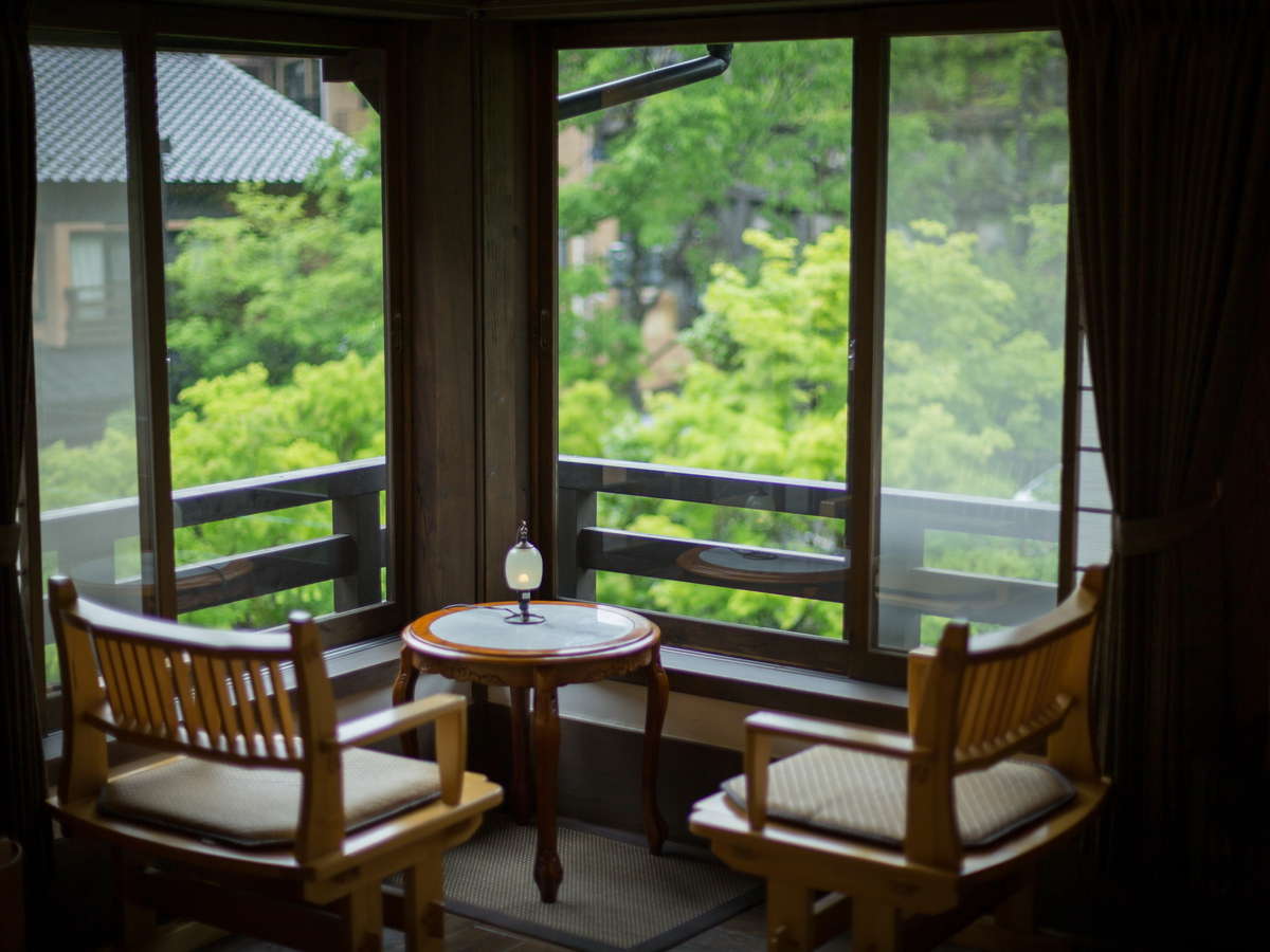 Bay-window sitting nook at Fujiya with two wooden chairs, a small candle-lit table and views over fresh green maples