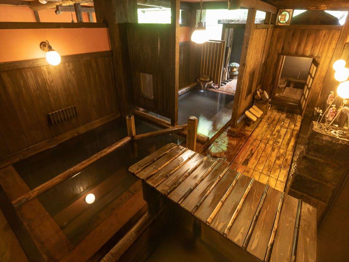 Rustic timber indoor bathhouse at Fujiya with stepped wooden tubs, bamboo duckboard floor and a corridor to a second bath