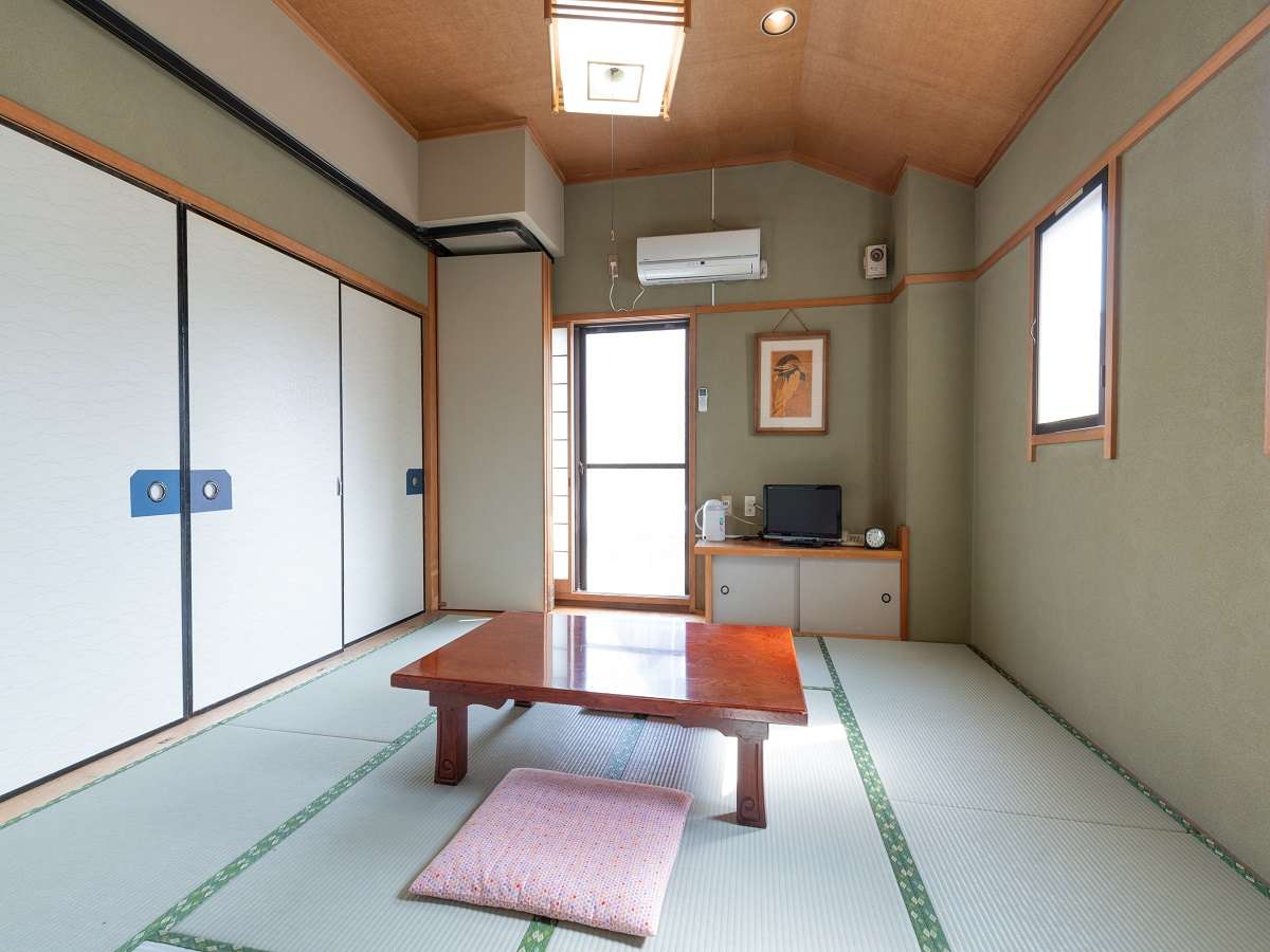 Spacious Japanese-style tatami guest room at Sakura Ryokan with a low table, floor cushion and balcony door